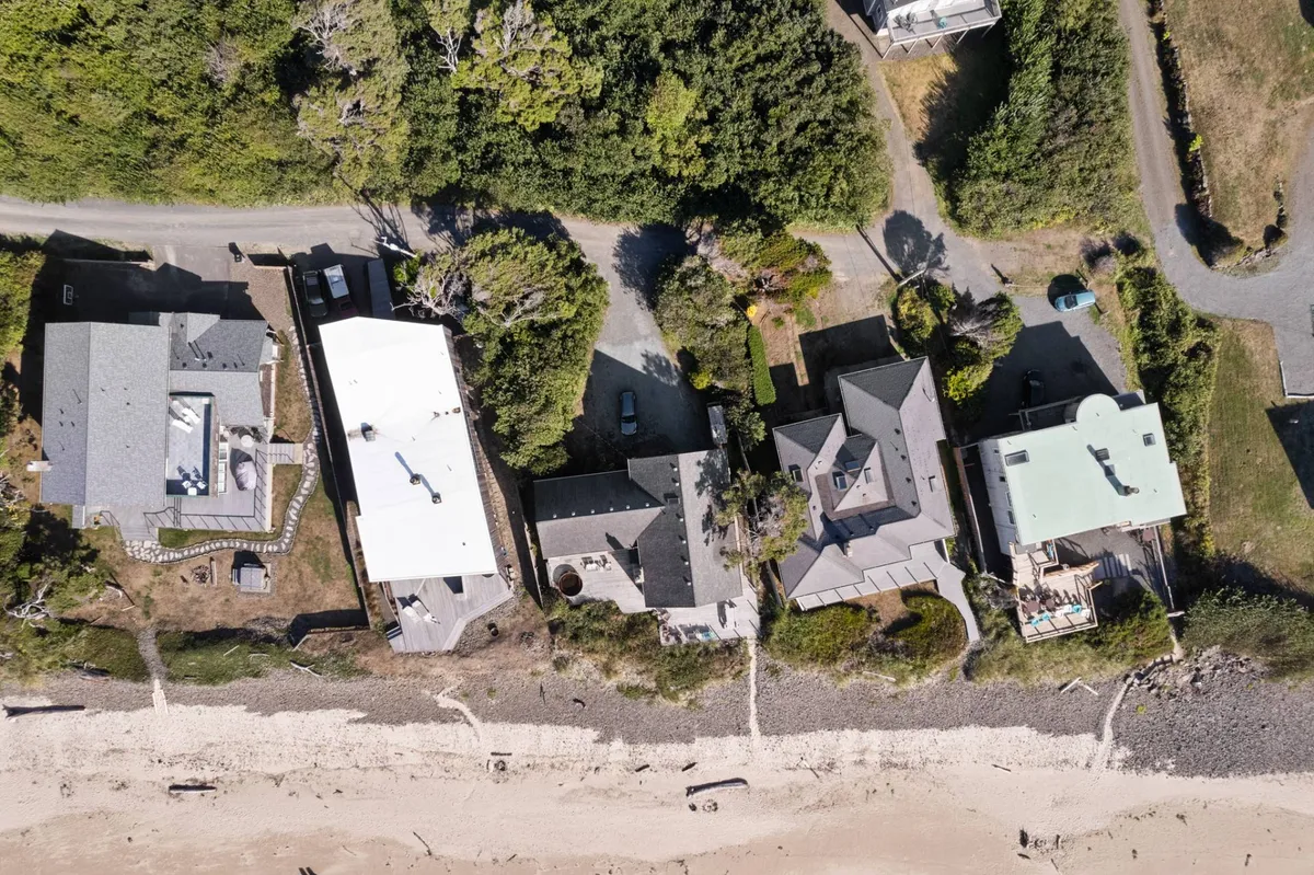 A broad view of beachfront properties framed by a tranquil tree line and walking paths, perfect for strolls and group outdoor activities. The beach is inviting and accessible, ideal for family walks or group outings.