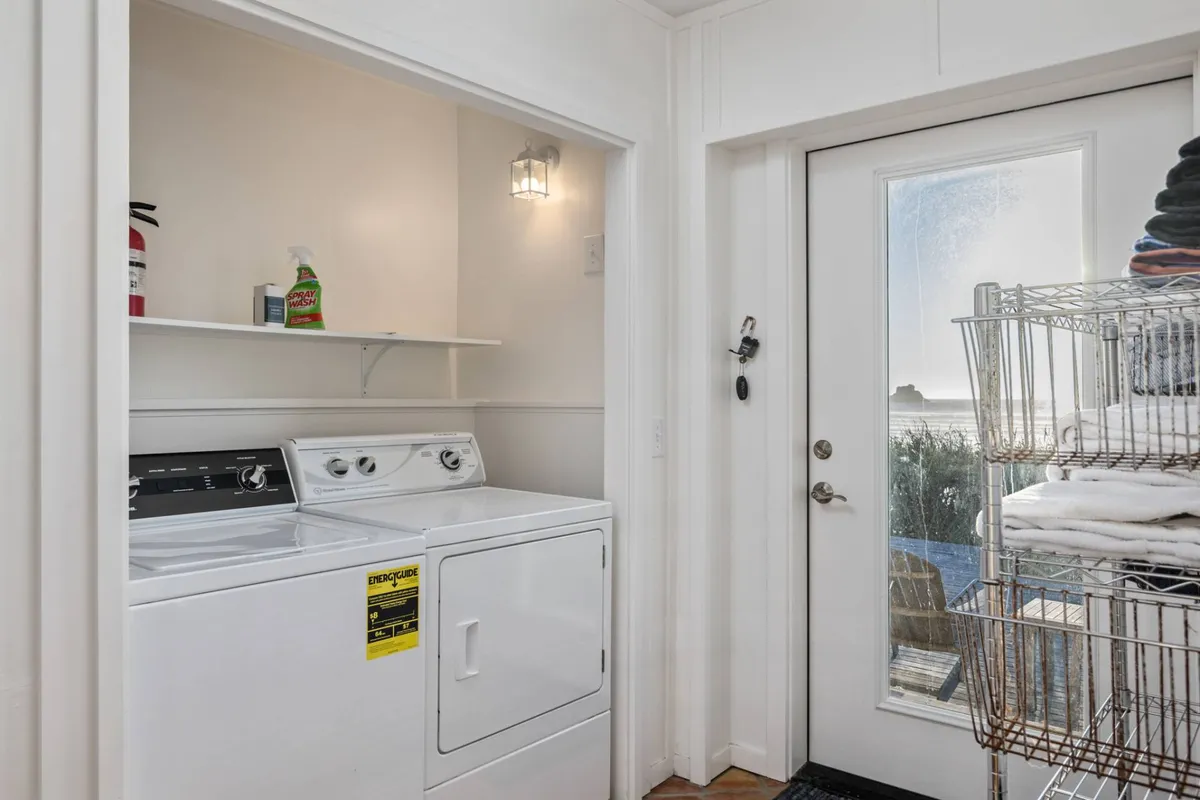 A functional laundry and mudroom with a washer, dryer, and a door leading outside. The space is neatly organized, featuring shelves with cleaning supplies and stacks of towels, while the exterior access door suggests convenience for families (and pets) coming in from outdoor adventures.
