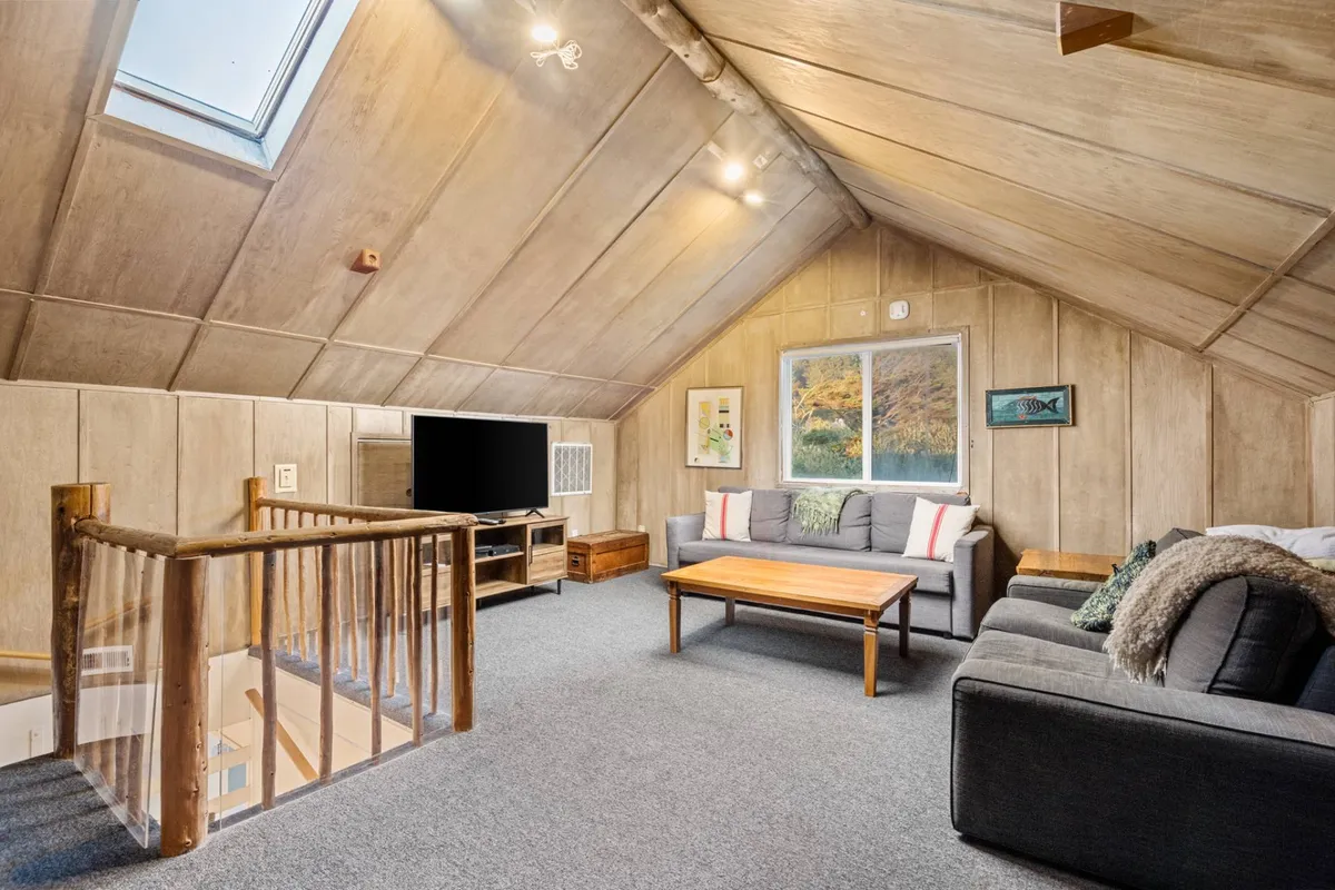 A welcoming loft area with a cozy sofa, coffee table, TV, and a window offering a pleasant view. The space is set up for relaxing, watching movies, or gathering with friends and family in a comfortable nook.