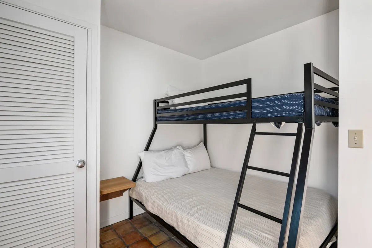 A cozy bunk room featuring a sturdy, stylish bunk bed, textured flooring, and a small side table. The room feels playful but also inviting, perfect for children or younger travelers seeking their own private space.