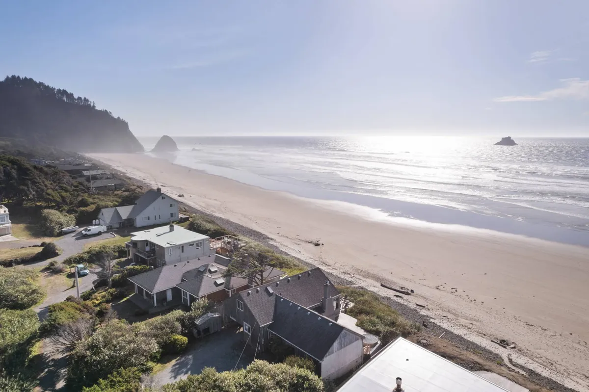 A sweeping ocean view with waves, a distant rock formation, and beachfront houses captures the wild beauty of the Pacific coast. The scene is vibrant and invites exploration, from beachcombing to sunset strolls along the shore.