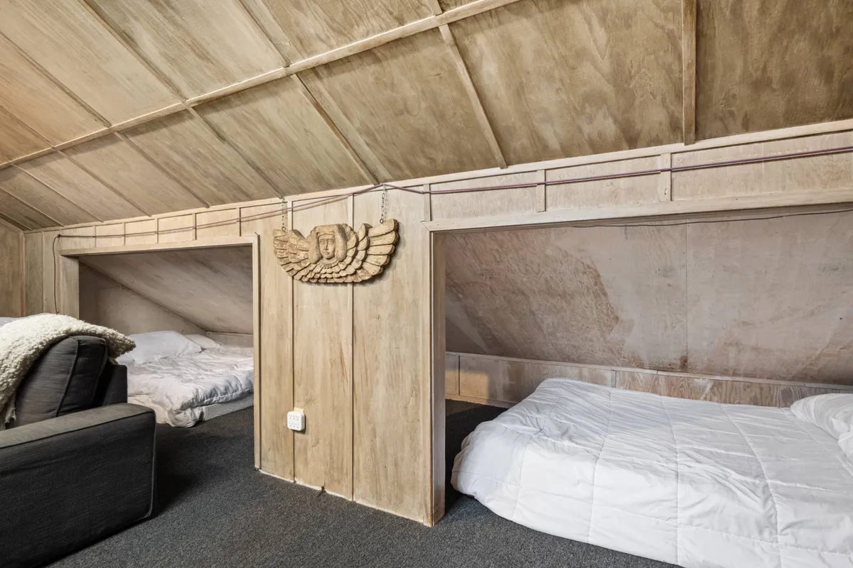 A warm, relaxed space with two sleeping areas separated by textured wooden walls, a comfortable sofa, and gentle lighting. The room exudes a feeling of comfort and togetherness, ideal for intimate conversations or relaxing with a book.