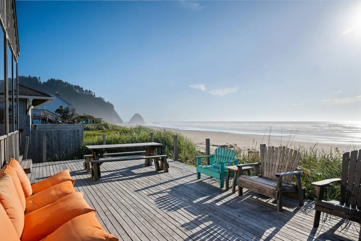 A tranquil deck scene with comfortable lounge seating and adirondack chairs arranged to maximize the panoramic ocean view. The wooden deck sits just above the sand, offering guests a peaceful spot to sunbathe, dine al fresco, or watch the sunrise and sunset.